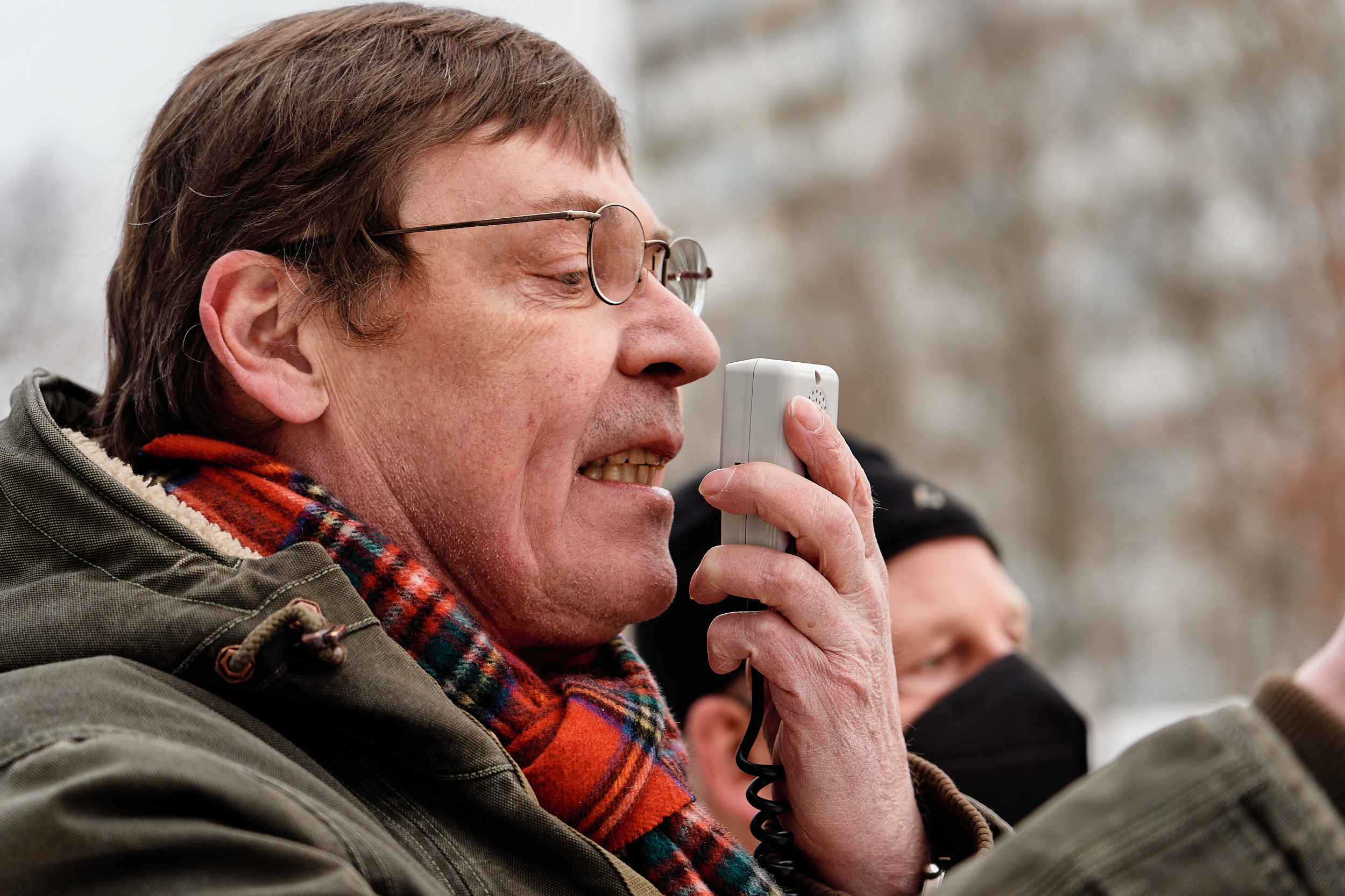 Ein Mann im Parka und mit Brille spricht während einer Kundgebung